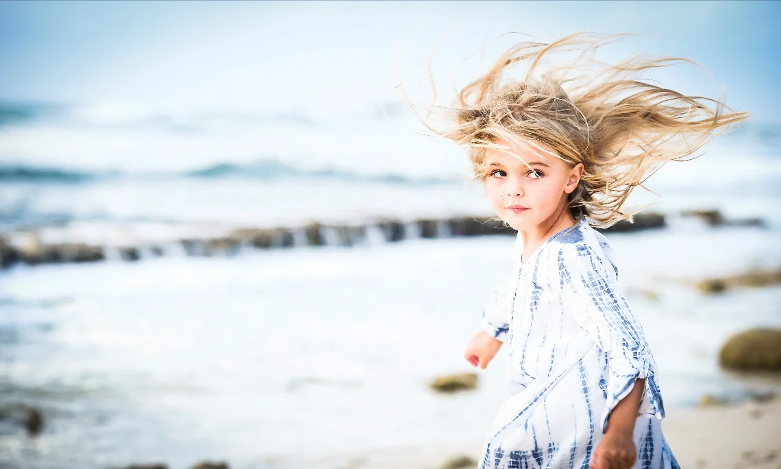 Girl in a blue and white dress with wind-swept hair on a Grand Cayman beach