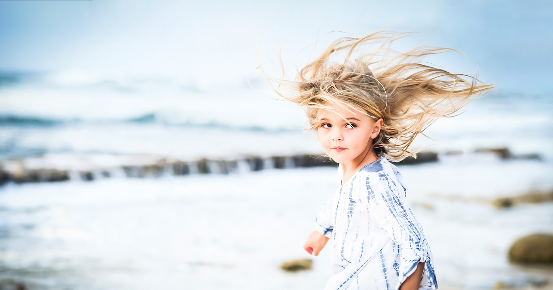 Girl in a blue and white dress with wind-swept hair on a Grand Cayman beach